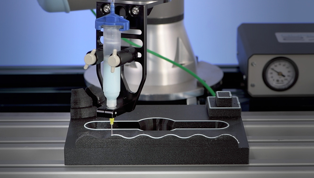 Adhesive dispensing robot syringe attachment applying adhesive to part with luer needle.